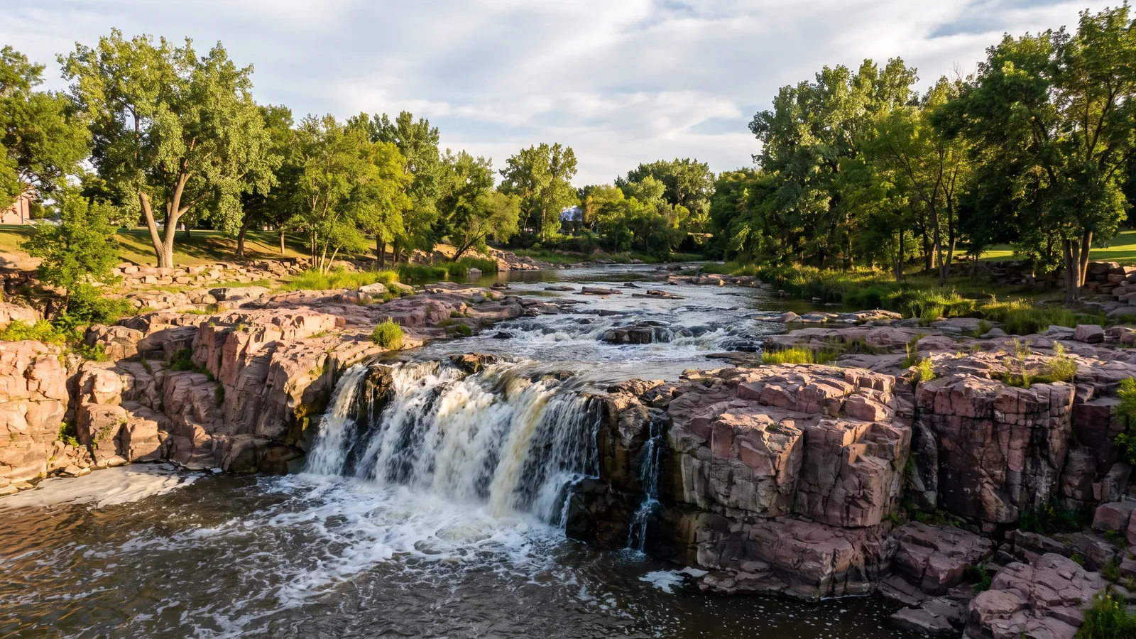The Big Sioux River pouring over pink Sioux quartzite at Falls Park with cottonwoods and ash along the banks